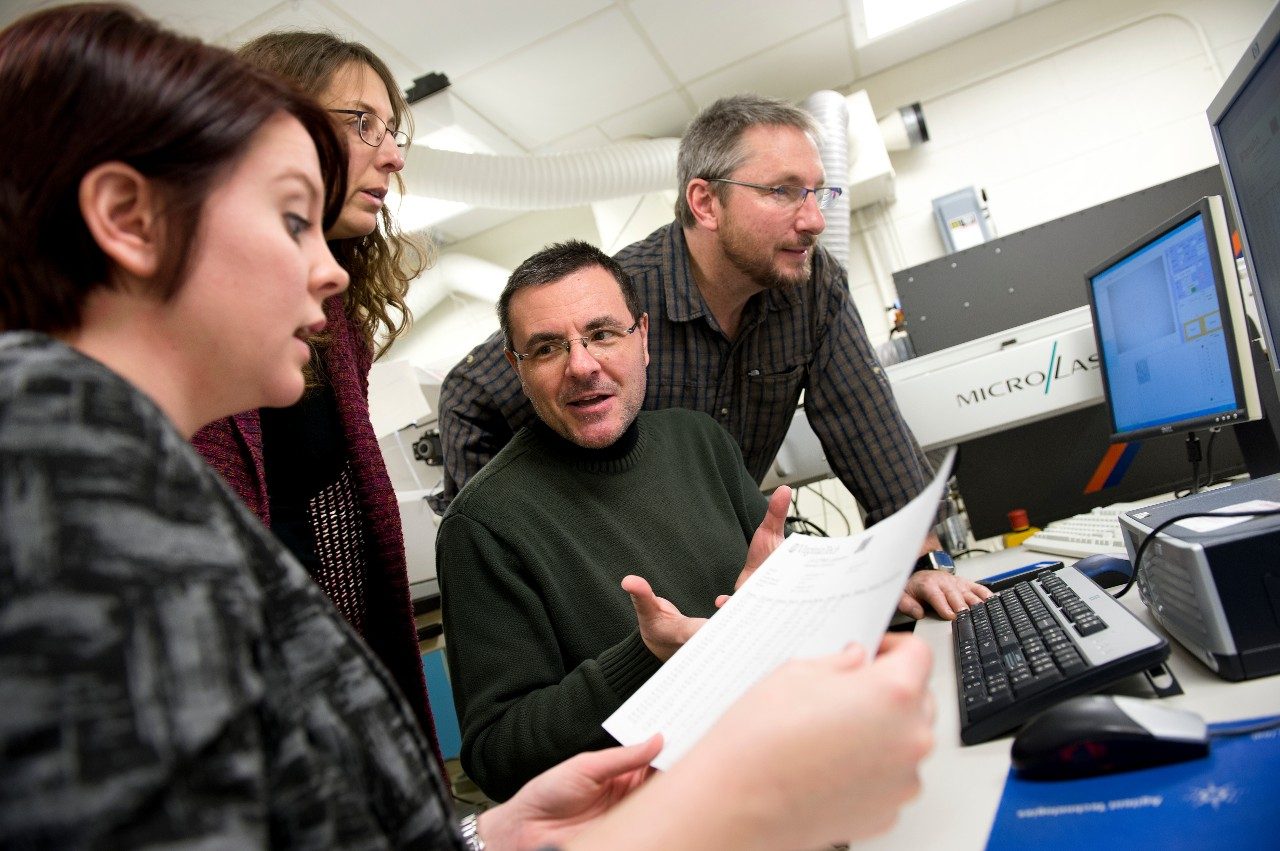 Close-up of four people in front of a monitor discussing results of a measurement