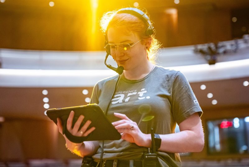Moss Arts Center Senior Technician CJ Jessie holds an iPad in the Anne and Ellen Fife Theatre as she controls the lighting.