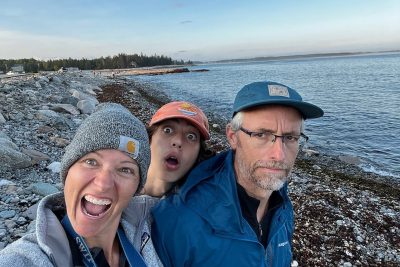 Flori Bliss (at left) standing with two people on an ocean coast. 