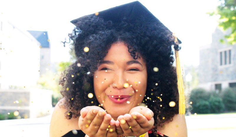 Graduate in cap and tassel blowing glitter from her hands.