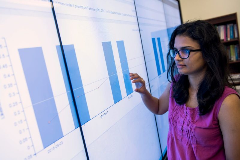 A researcher pointing at a large screen, screen is featuring bar graphs.