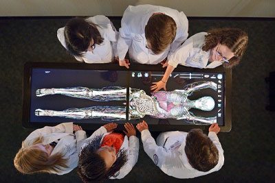 Medical students standing over an Anatomage Table.
